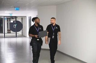 Två tekniker från Addici går genom en korridor med varsin laptop i händerna.