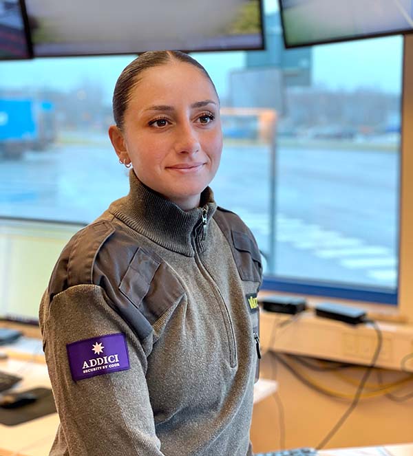 En väktare från Addici framför ett stort fönster med bildskärmar ovanför.