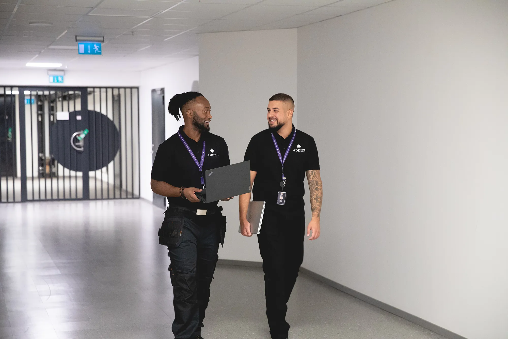 Två av Addicis tekniker går genom en korridor med laptops
