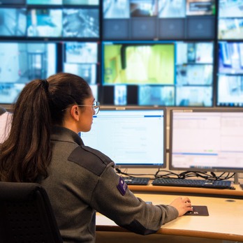 En operatör på Addicis larmcentral vid skrivbord framför en vägg med många skärmar