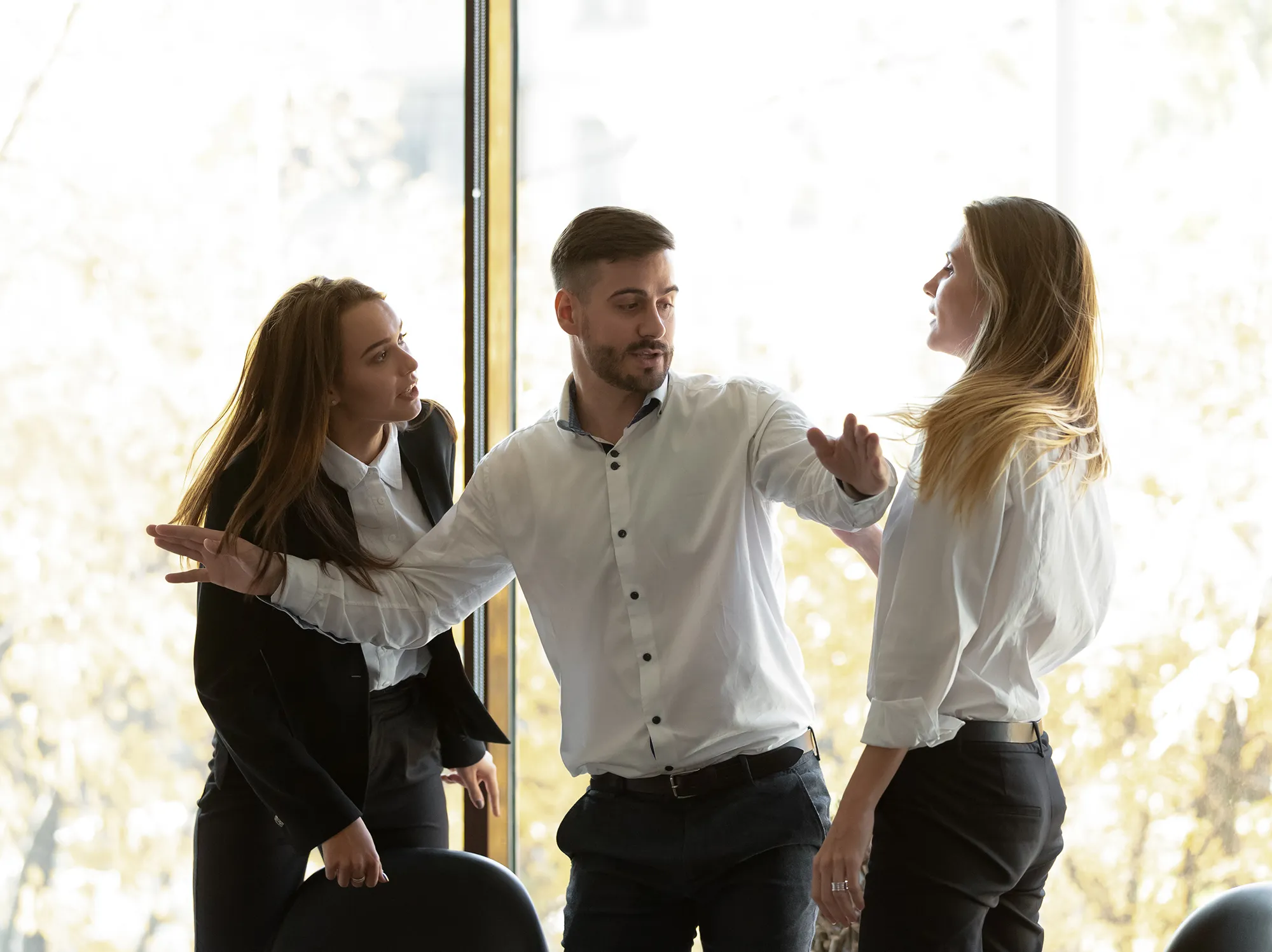 En man går emellan två kvinnor i en konflikt på ett kontor