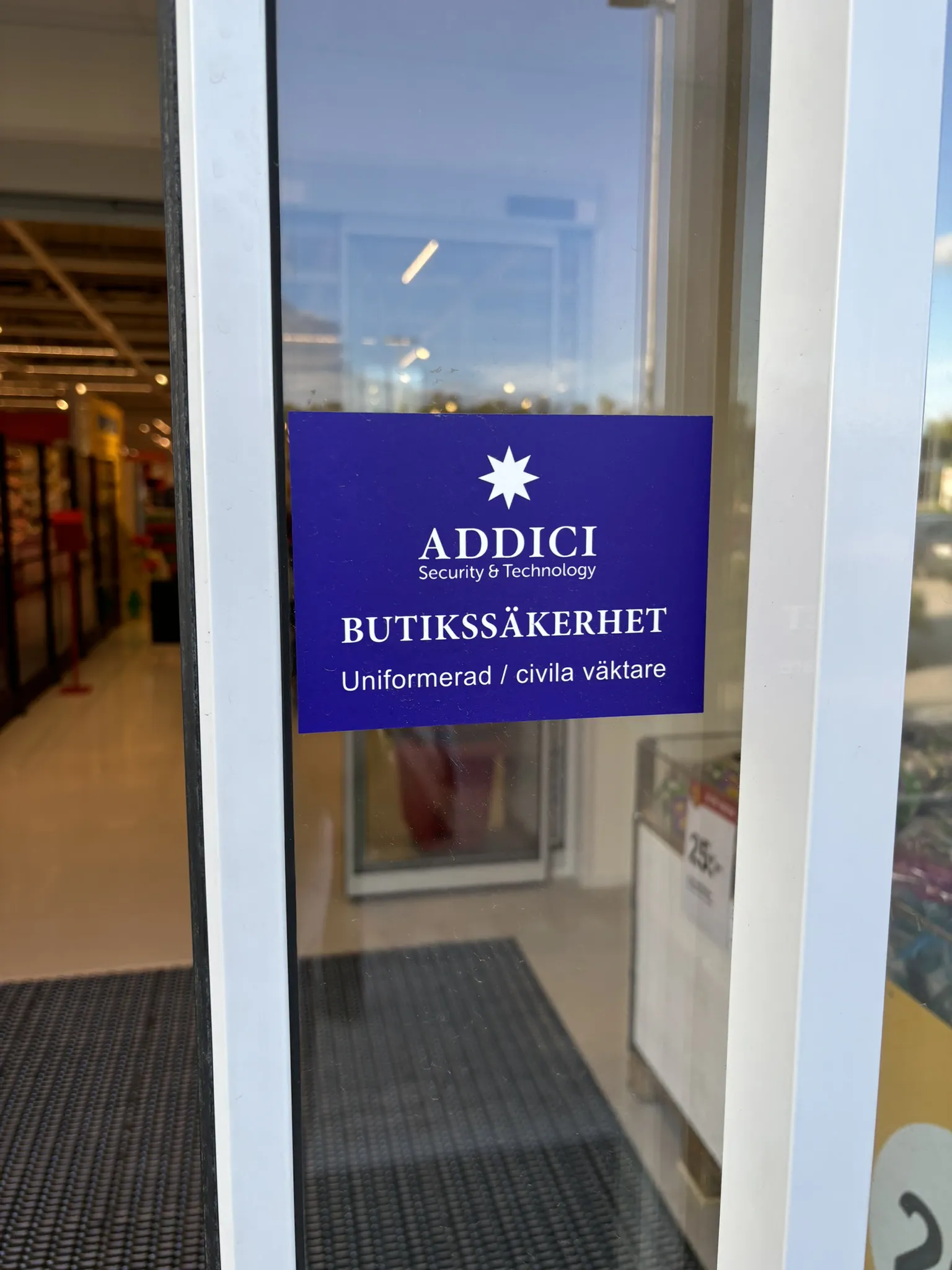 En entredörr till en butik med lila skylt som berättar att Addicis civila och uniformerade väktare ansvarar för butikssäkerheten